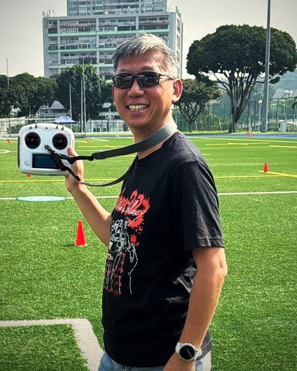 Bernard Neo smiling, holding a remote controller, on a sports field in Singapore