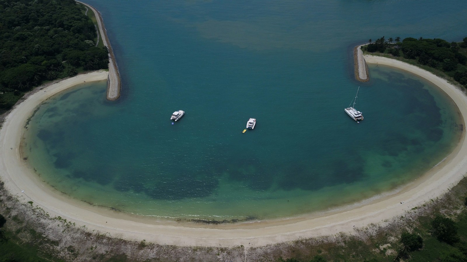 Curved white-sand beach on Lazarus Island seen from above, with boats anchored in the lagoon