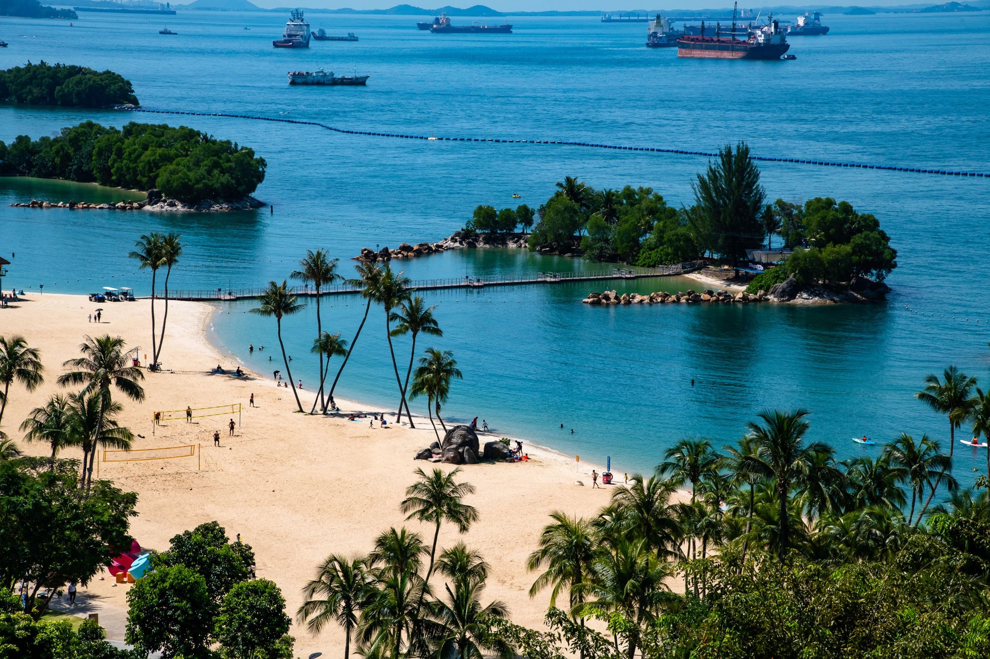 Palm-lined beach on Sentosa with small offshore islets and ships at anchor